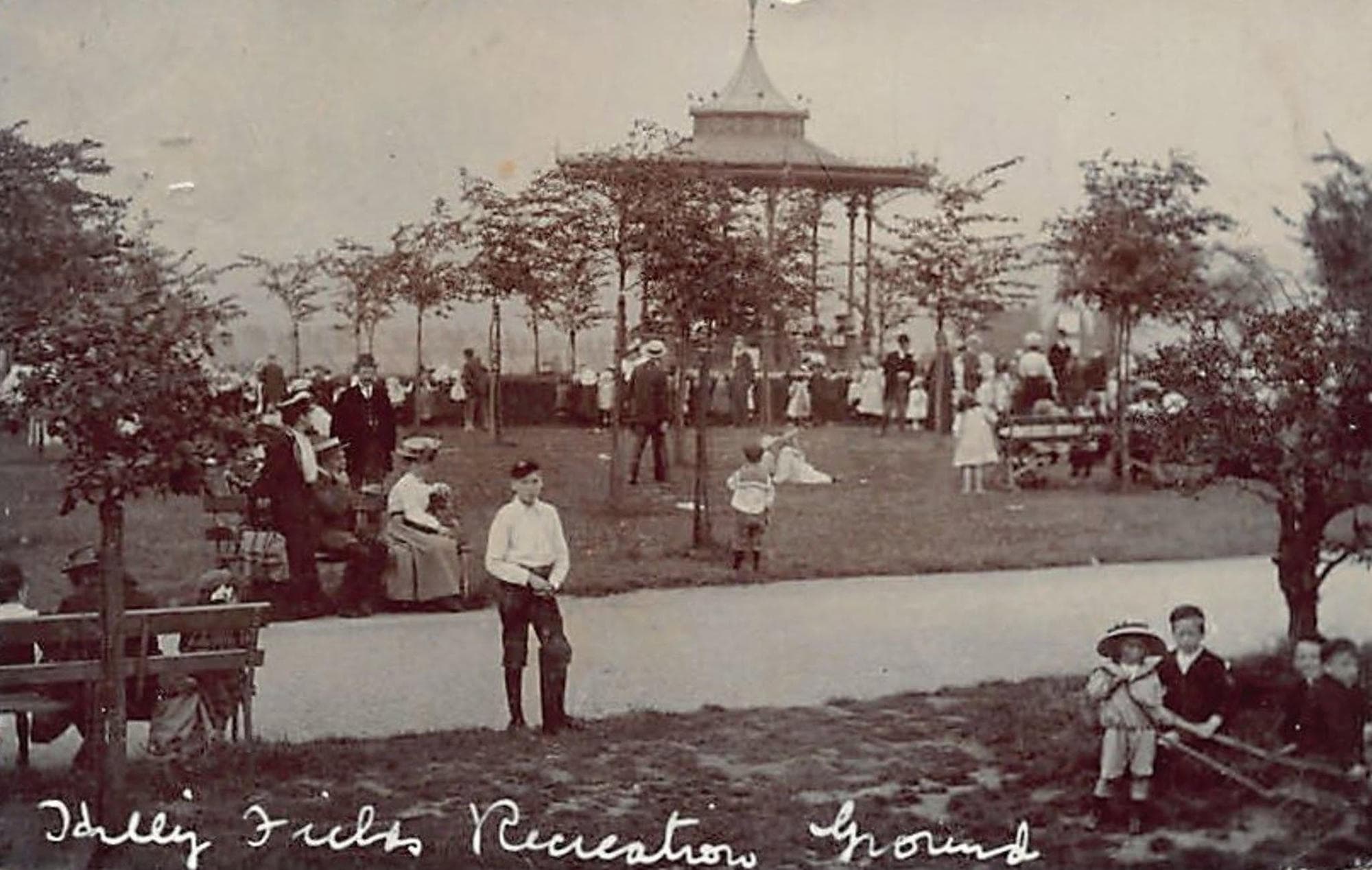 Edwardian postcard of Hilly Fields Recreation Ground, showing a large crowd gathered around the bandstand among young trees